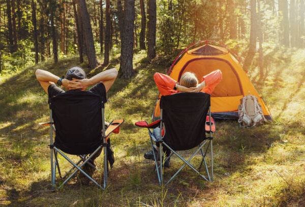 people relaxing in camping chairs at forest campsite and enjoying the nature