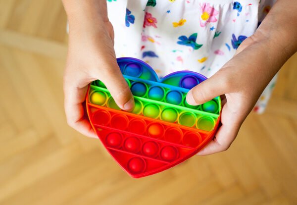 Girl holding heart shaped rainbow pop it toy. New fidget trendy toy. Antistress toy. Simple dimple.